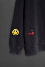 Detalle del bordado carita feliz y cerezas en la manga del buzo negro washed
