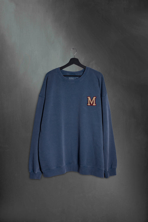 Buzo azul washed oversize con M bordada estilo varsity de Mushkana