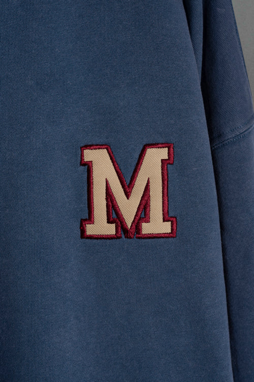 Detalle de la M bordada estilo varsity en buzo azul washed