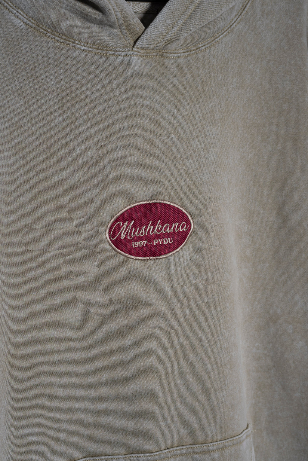Detalle del bordado Mushkana en el pecho del hoodie khaki washed